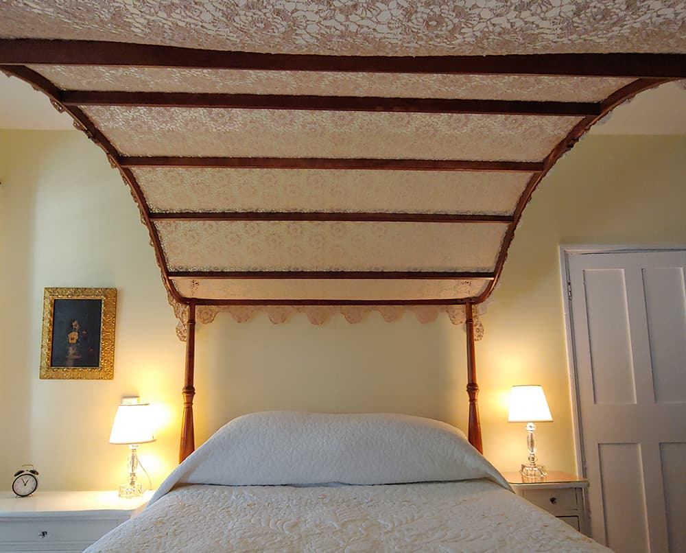 A canopy bed with a floral-patterned top under soft lighting in a cozy bedroom.